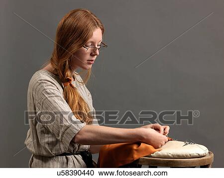 Stock Image - Young female designer sewing fabric on cushion. Fotosearch