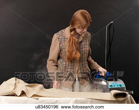 Stock Photograph - Young female designer steam ironing fabric. Fotosearch