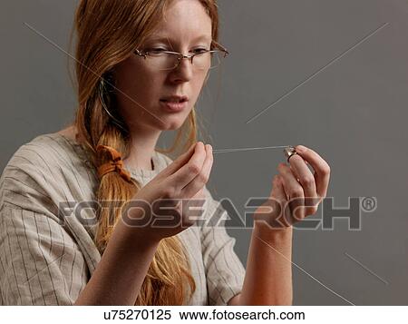 Stock Photography - Young female designer threading a sewing needle. Fotosearch