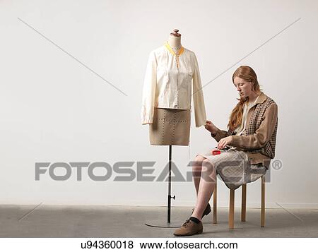 Young female fashion designer sitting on stool pinning blouse on dressmaker's dummy View Large Photo Image Stock Photo - Young female fashion designer sitting on stool pinning blouse on dressmaker's dummy. Fotosearch