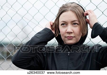 Stock Photo - Young female runner in black hoody by wire fence. Fotosearch