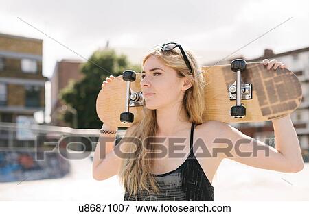 Stock Photo - Young female skateboarder carrying skateboard on shoulders in skatepark. Fotosearch