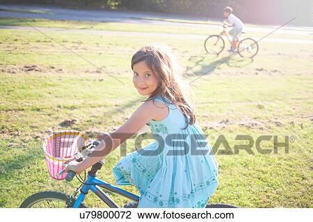Stock Image - Young girl and boy riding bike in summer sun. Fotosearch