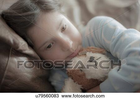 Young girl lying on sofa, hugging soft toy, sad expression View Large Photo Image Stock Image - Young girl lying on sofa, hugging soft toy, sad expression. Fotosearch