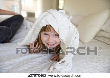 Young girl peeking head out from under blanket on bed View Large Photo Image Stock Image - Young girl peeking head out from under blanket on bed. Fotosearch