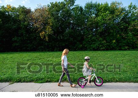 Stock Photography - Young girl riding her bicycle followed by mother. Fotosearch