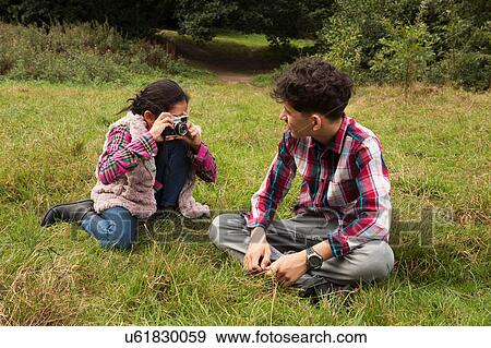 Young girl, sitting in field, photographing brother, using camera View Large Photo Image Stock Photo - Young girl, sitting in field, photographing brother, using camera. Fotosearch