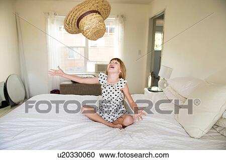 Young girl sitting on bed, throwing straw hat up in air View Large Photo Image Stock Image - Young girl sitting on bed, throwing straw hat up in air. Fotosearch