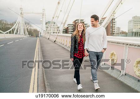 Stock Photograph - Young happy couple strolling on bridge, Battersea Park, London, UK. Fotosearch