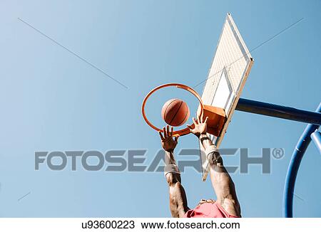 Stock Image - Young male basketball player throwing ball in basketball hoop. Fotosearch