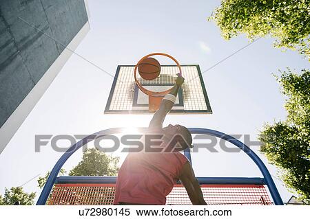 Young male basketball player throwing ball in sunlit basketball hoop View Large Photo Image Stock Photography - Young male basketball player throwing ball in sunlit basketball hoop. Fotosearch