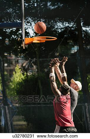 Stock Image - Young male basketball players throwing ball at basketball hoop. Fotosearch