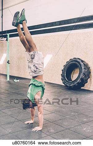 Picture - Young male cross trainer doing handstand in gym. Fotosearch