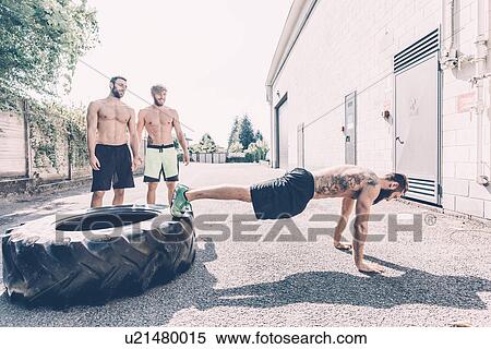 Stock Photography - Young male cross trainer doing push-ups from tyre outside gym. Fotosearch