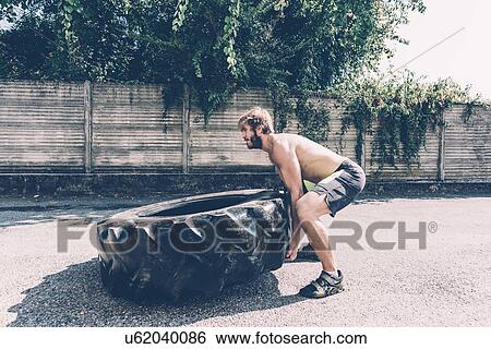 Young male cross trainer lifting heavy tyre outside gym View Large Photo Image Stock Photograph - Young male cross trainer lifting heavy tyre outside gym. Fotosearch