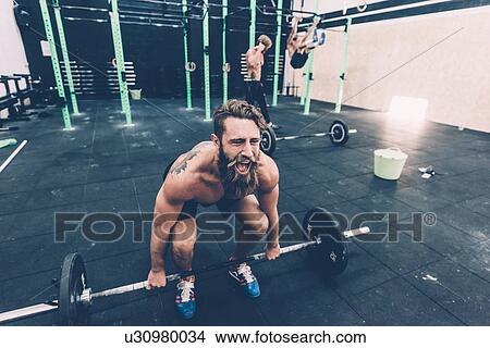 Young male cross trainer preparing to lift barbell in gym View Large Photo Image Picture - Young male cross trainer preparing to lift barbell in gym. Fotosearch