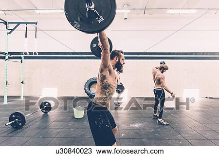 Stock Image - Young male cross trainer snatch lifting barbell in gym. Fotosearch