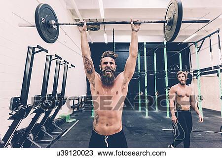 Stock Image - Young male cross trainer snatch lifting barbell in gym. Fotosearch