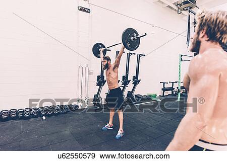 Stock Photo - Young male cross trainer snatch lifting barbell in gym. Fotosearch