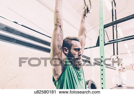 Stock Image - Young male cross trainer training on exercise rings in gym. Fotosearch