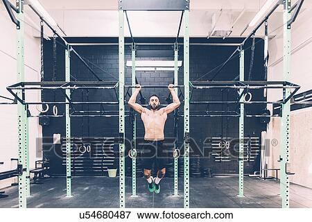 Stock Photo - Young male cross trainer training on exercise bar in gym. Fotosearch