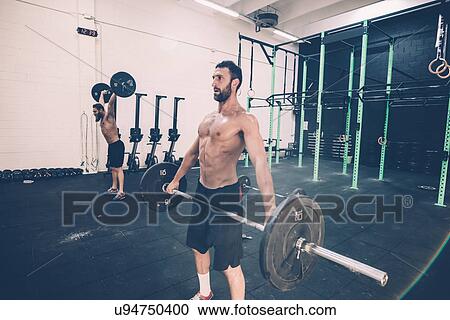 Stock Image - Young male cross trainer weightlifting barbell in gym. Fotosearch