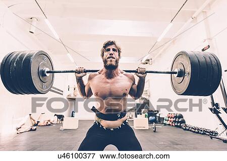Stock Photo - Young male cross trainer weightlifting barbell in gym. Fotosearch