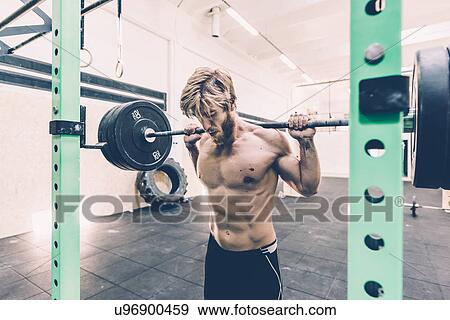 Stock Photo - Young male cross trainer weightlifting barbell in gym. Fotosearch