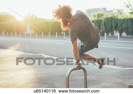 Stock Photograph - Young male hipster kicking up heels on sunlit sidewalk. Fotosearch