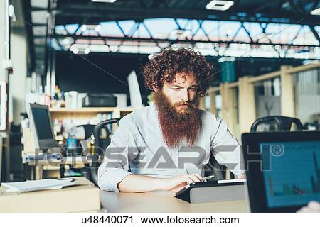 Stock Image - Young male hipster using digital tablet at desk. Fotosearch