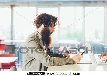Young male hipster with curly hair and beard using digital tablet at desk View Large Photo Image Stock Photo - Young male hipster with curly hair and beard using digital tablet at desk. Fotosearch