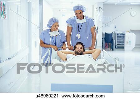 Stock Image - Young male patient in hospital bed being pushed by nurses. Fotosearch