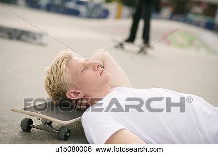 Stock Photograph - Young male skateboarder lying in skatepark with eyes closed. Fotosearch