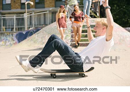 Young male skateboarder sitting on skateboard on the move in city skatepark View Large Photo Image Stock Image - Young male skateboarder sitting on skateboard on the move in city skatepark. Fotosearch