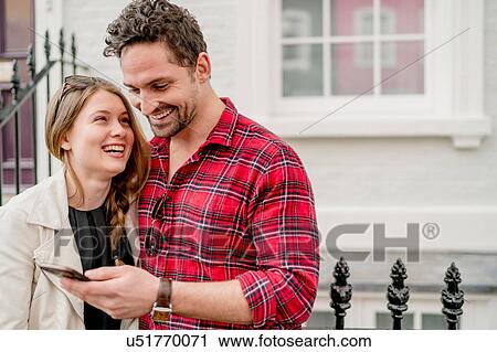 Stock Image - Young man and girlfriend reading smartphone texts, Kings Road, London, UK. Fotosearch
