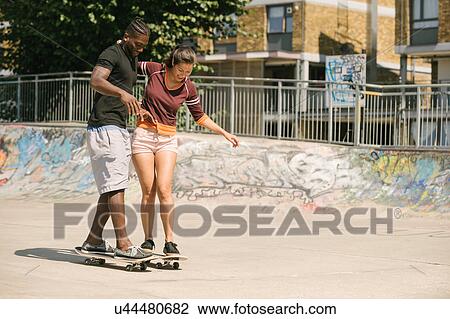 Stock Image - Young man and woman practising skateboarding balance in skatepark. Fotosearch