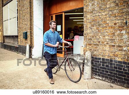 Young man carrying coffee and wheeling pushbike past workshop View Large Photo Image Stock Photograph - Young man carrying coffee and wheeling pushbike past workshop. Fotosearch