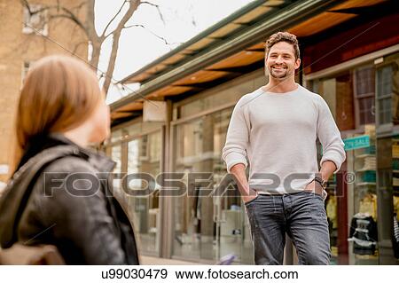 Stock Photo - Young man greeting girlfriend sitting on bench, Kings Road, London, UK. Fotosearch