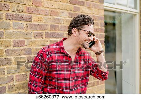 Stock Photo - Young man in front of brick wall talking on smartphone. Fotosearch