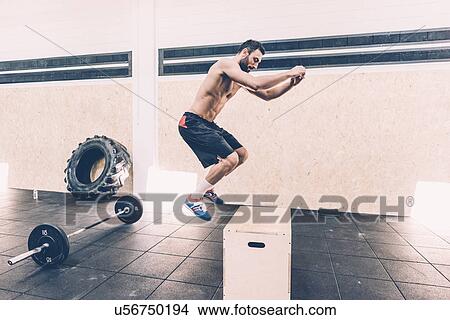 Picture - Young man jumping on box in cross training gym. Fotosearch