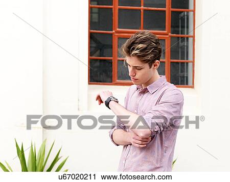 Young man looking at watch, outdoors View Large Photo Image Stock Image - Young man looking at watch, outdoors. Fotosearch