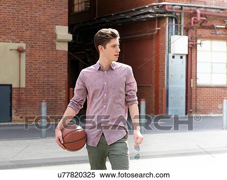 Young man outdoors, holding basketball and sunglasses, looking away View Large Photo Image Stock Photography - Young man outdoors, holding basketball and sunglasses, looking away. Fotosearch