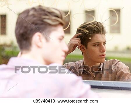 Stock Image - Young man outdoors, leaning against mirrored window, looking away. Fotosearch
