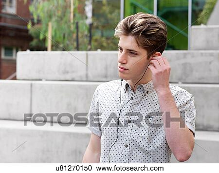 Stock Image - Young man outdoors, wearing earphones. Fotosearch