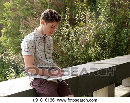 Stock Photograph - Young man outdoors, writing notes in notepad. Fotosearch