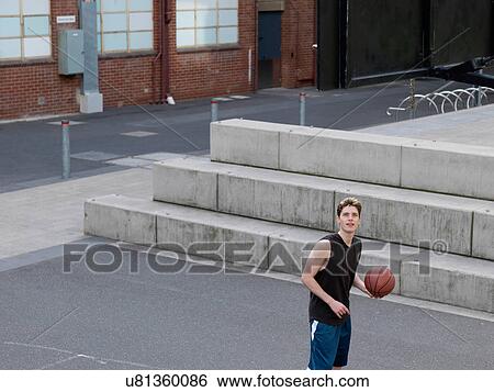 Stock Photograph - Young man playing basketball in outdoor court. Fotosearch