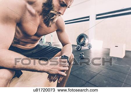 Young man sitting checking smartwatch in cross training gym View Large Photo Image Stock Image - Young man sitting checking smartwatch in cross training gym. Fotosearch