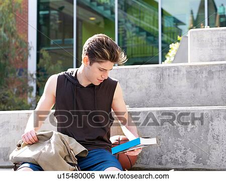 Stock Photograph - Young man sitting on step, outdoors, reading back of book. Fotosearch