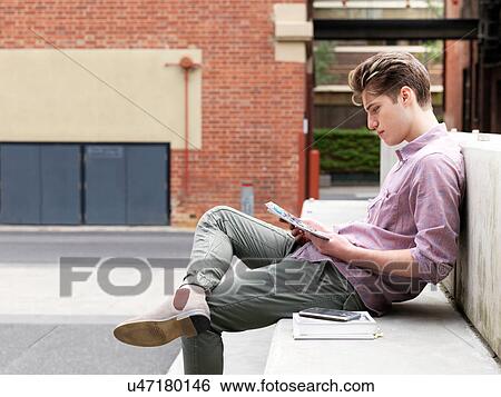 Young man sitting on step, outdoors, reading book View Large Photo Image Stock Photograph - Young man sitting on step, outdoors, reading book. Fotosearch