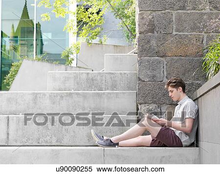 Stock Photography - Young man sitting on step, outdoors, writing in notepad. Fotosearch
